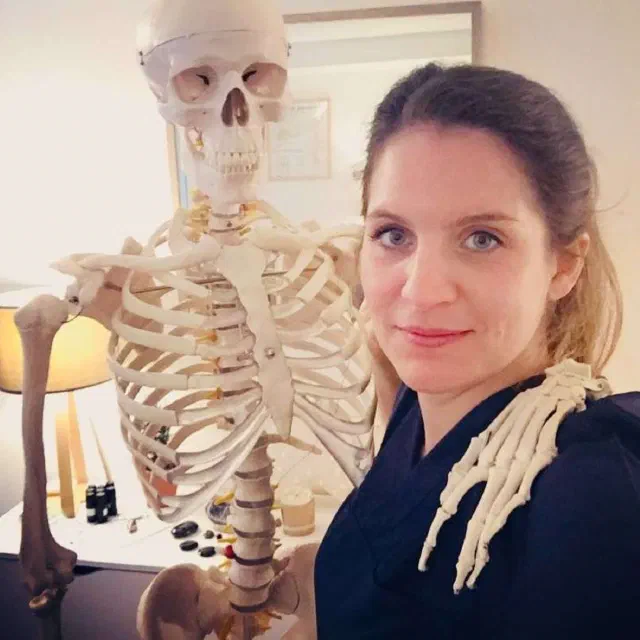Caroline Sabaty, ostéopathe, souriante dans son cabinet de Levallois-Perret, à côté d’un squelette anatomique
